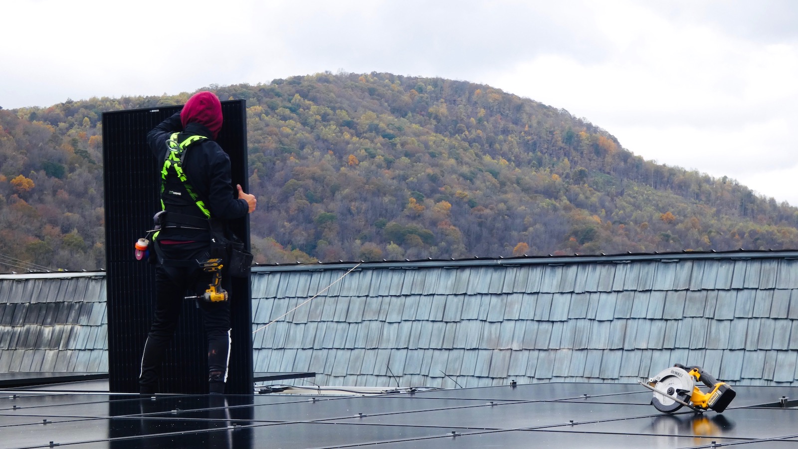 A solar installer positions a photovoltaic panel on the roof of Iron Works Cycling in Big Stone Gap, Virginia.