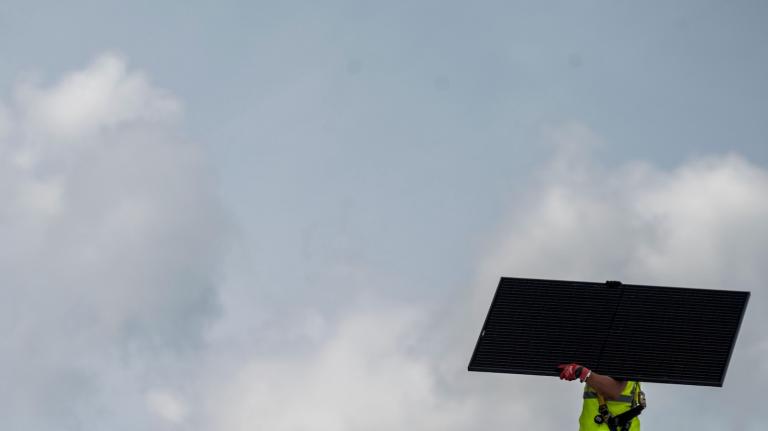 A man carrying a solar panel works on the roof of a church in Alexandria, Virginia.