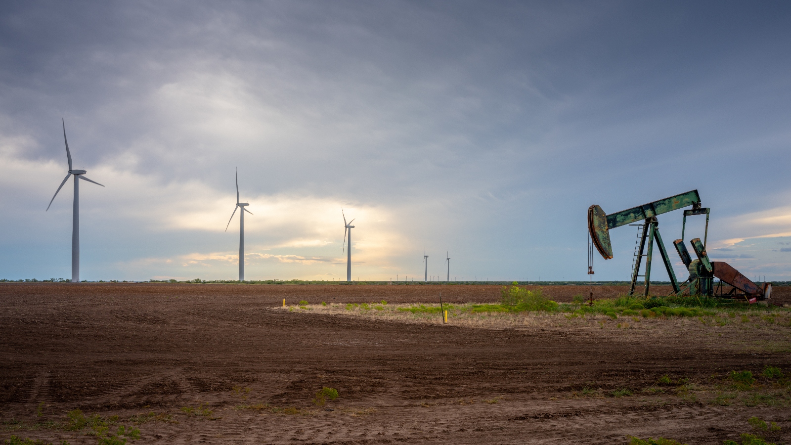 An oil pumpjack near a field of wind turbines.