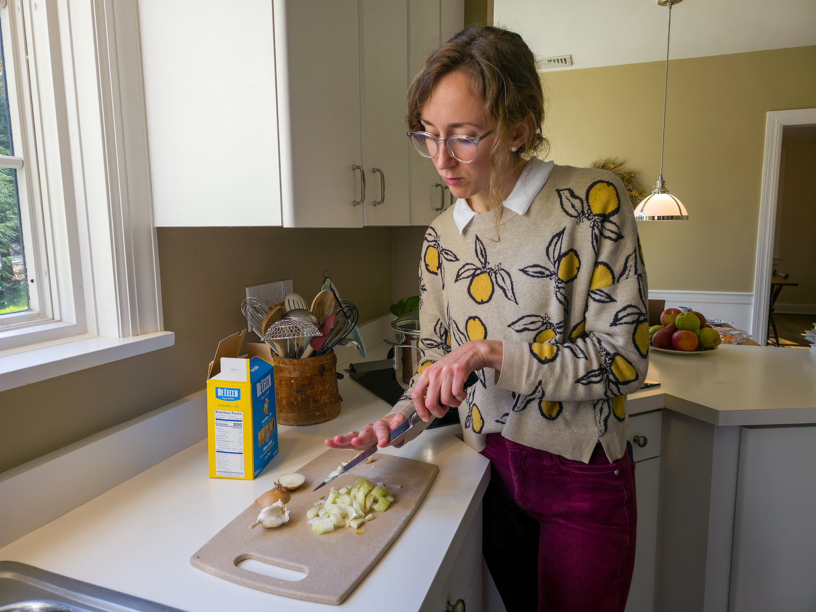 a woman in a lemon-print sweater cops onions in a kitchen