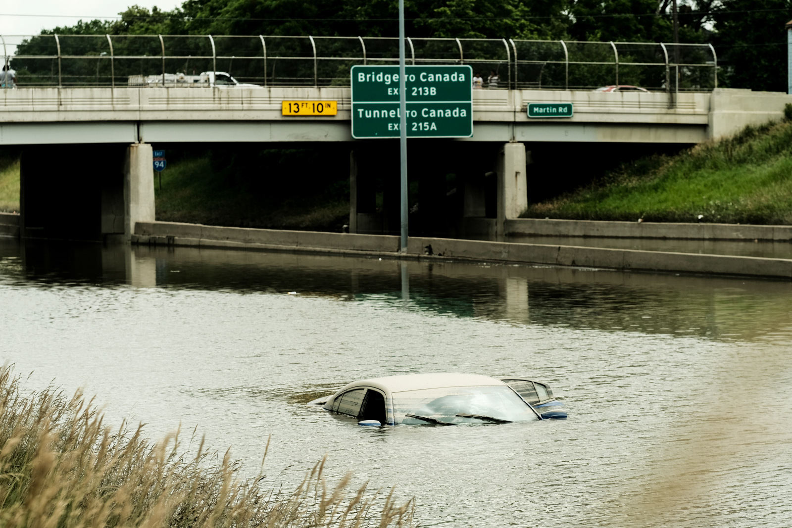 Photo of a car nearly covered by floodwaters near a highway overpass