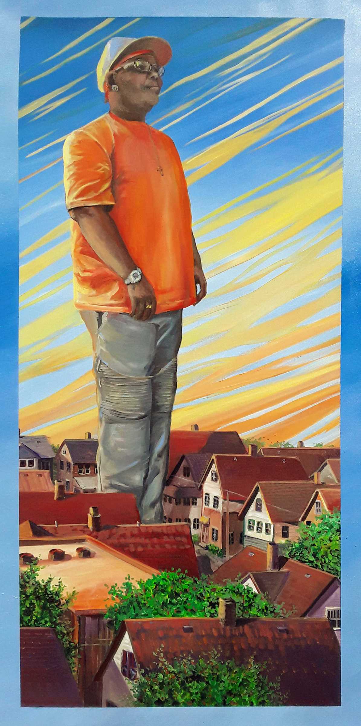 A painting of a Black woman wearing an orange T-shirt, jeans, and a baseball cap, standing tall above the buildings of a town.