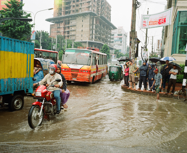 Motorcyclists and buses in a flooded Dhaka street