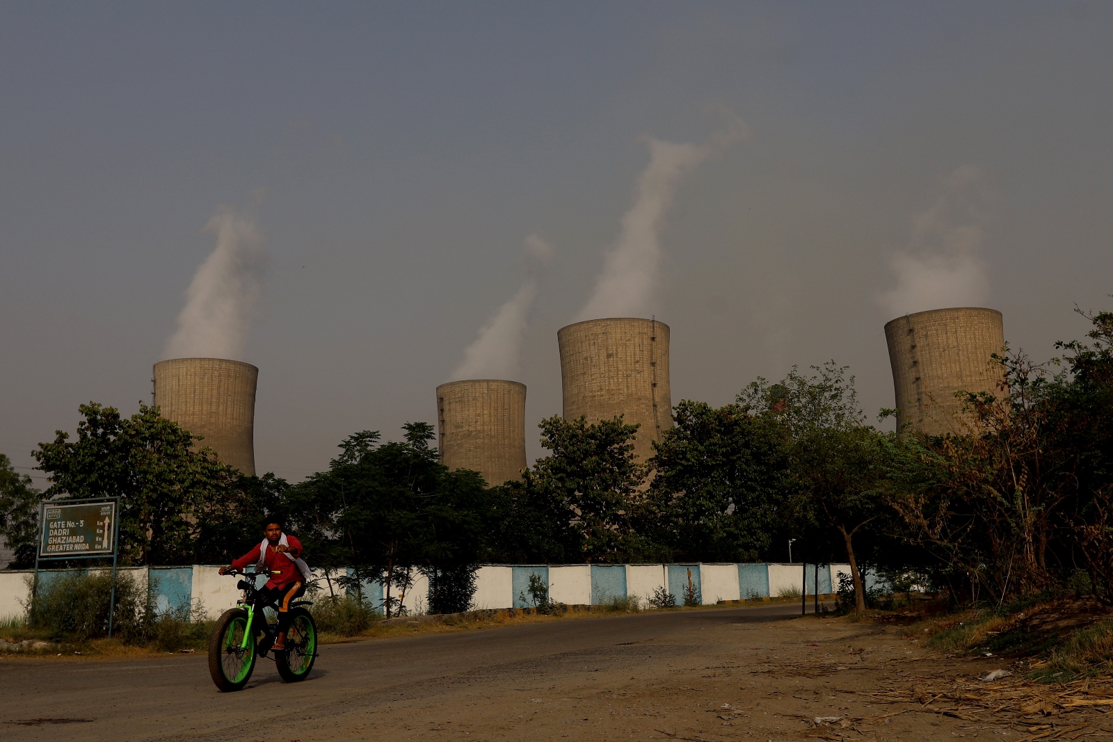 An Indian man rides a bike in front of the National Thermal Power Corporation coal-fired power plant in the Gautam Budh Nagar district of Ghaziabad, India.