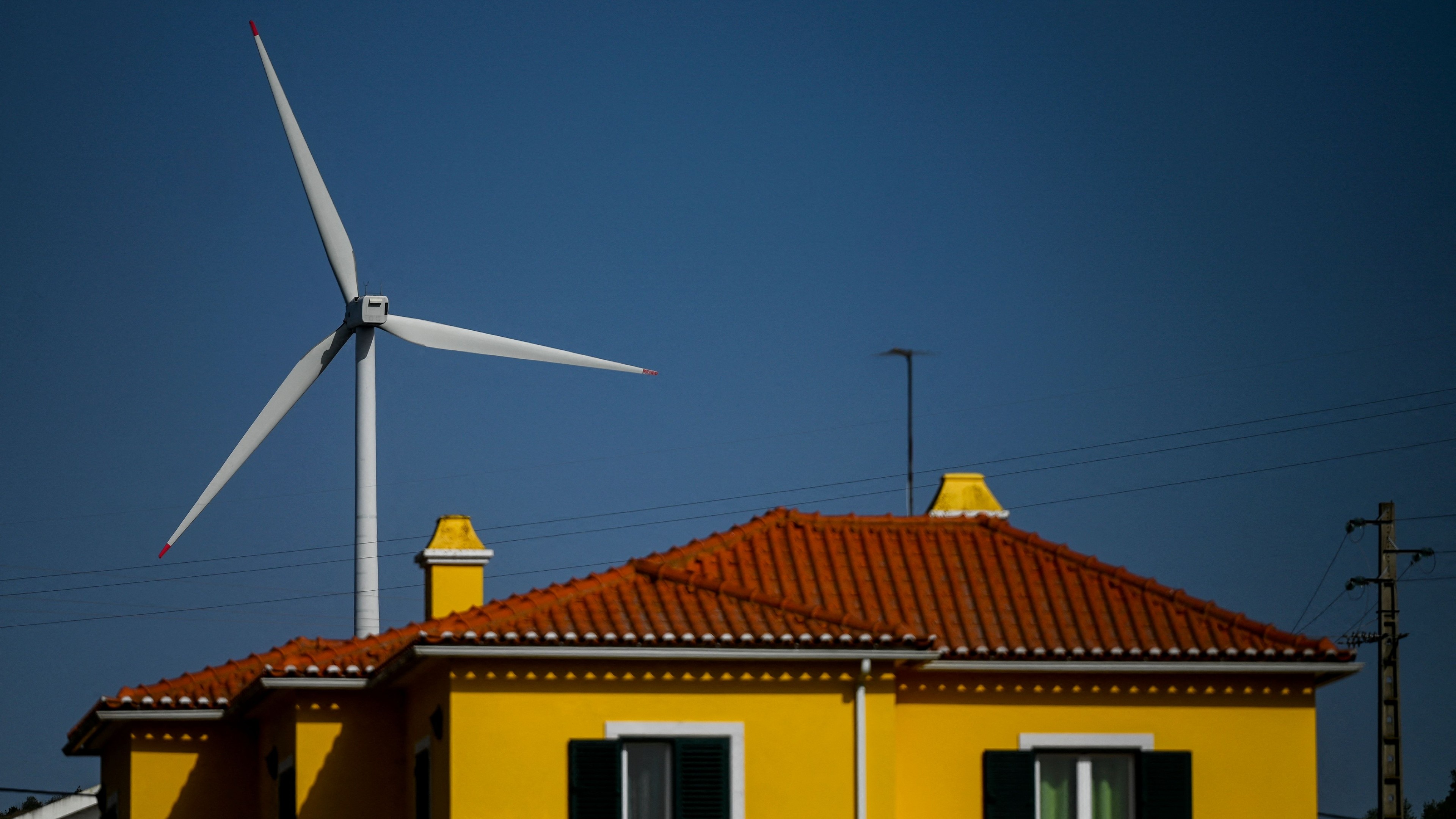 A huge wind turbine sticks out behind a yellow house with red terracotta roof tiles.