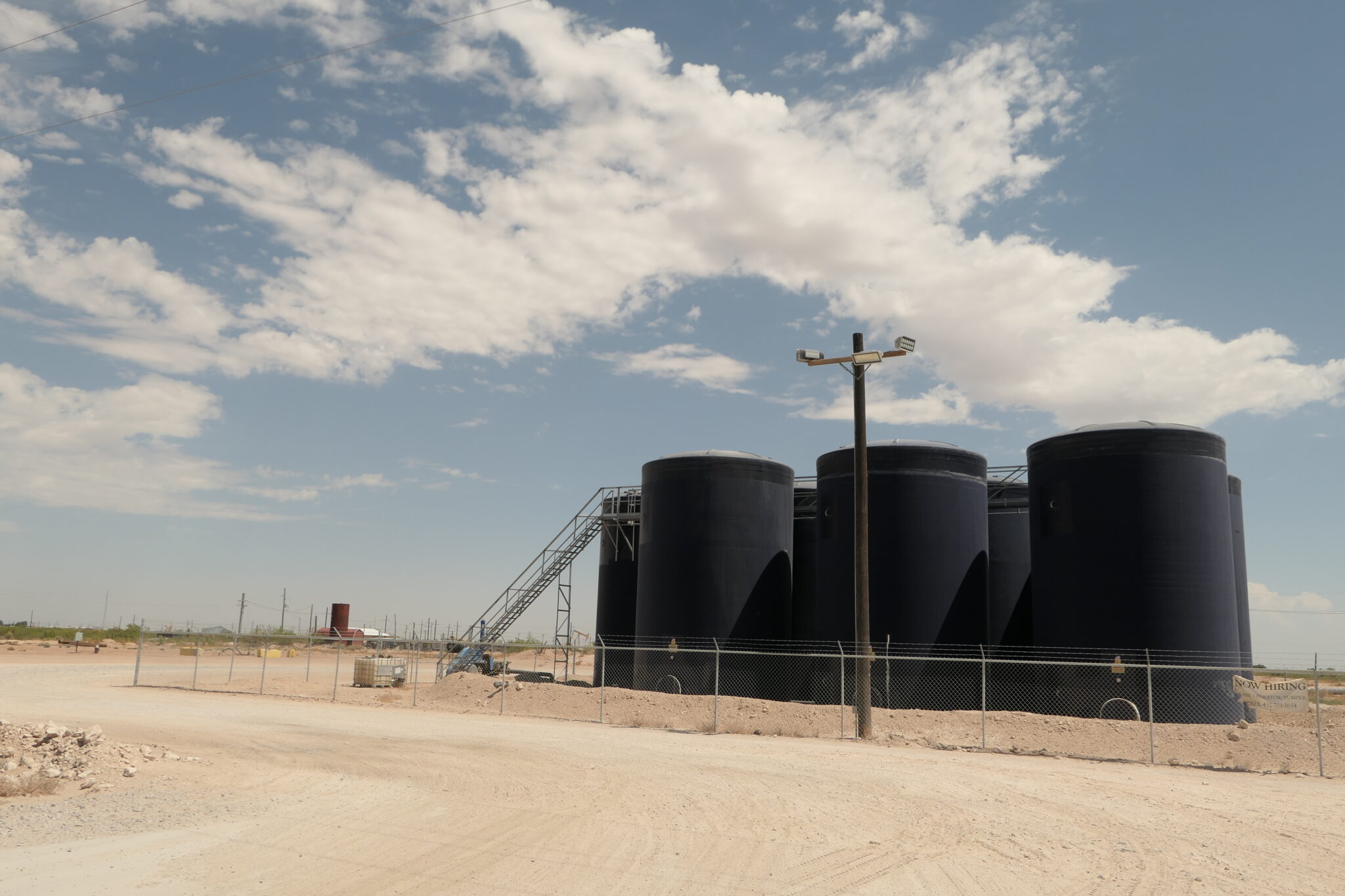 A series of huge black tanks sit in the desert under a blue sky.