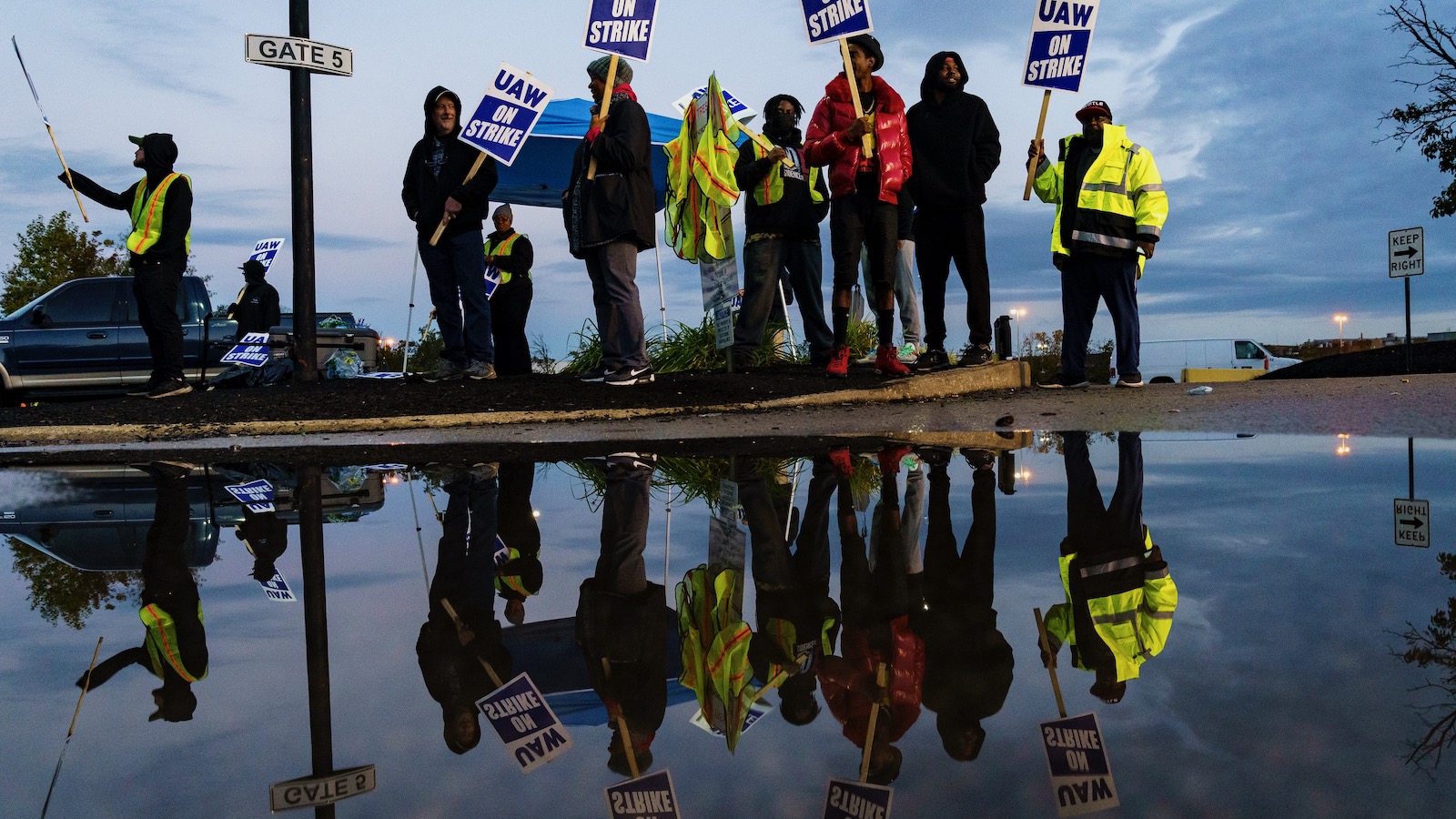 Factory workers and members of the United Auto Workers waving placards outside a factory in Louiseville, Kentucky are reflected in a puddle.