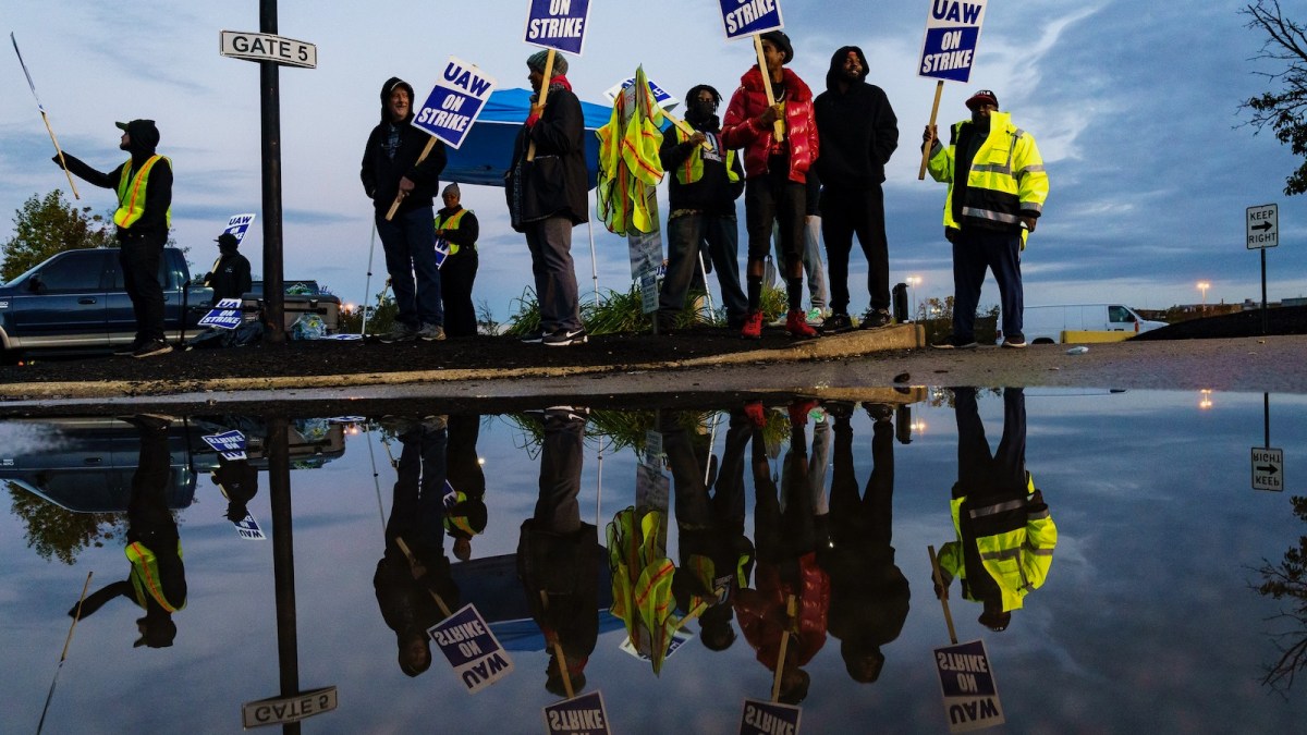 Factory workers and members of the United Auto Workers waving pickets outside a factory in Louiseville, Kentucky, are reflected in a puddle.
