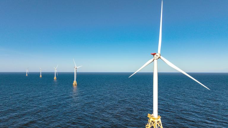 A line of wind turbines in the ocean under a blue sky.