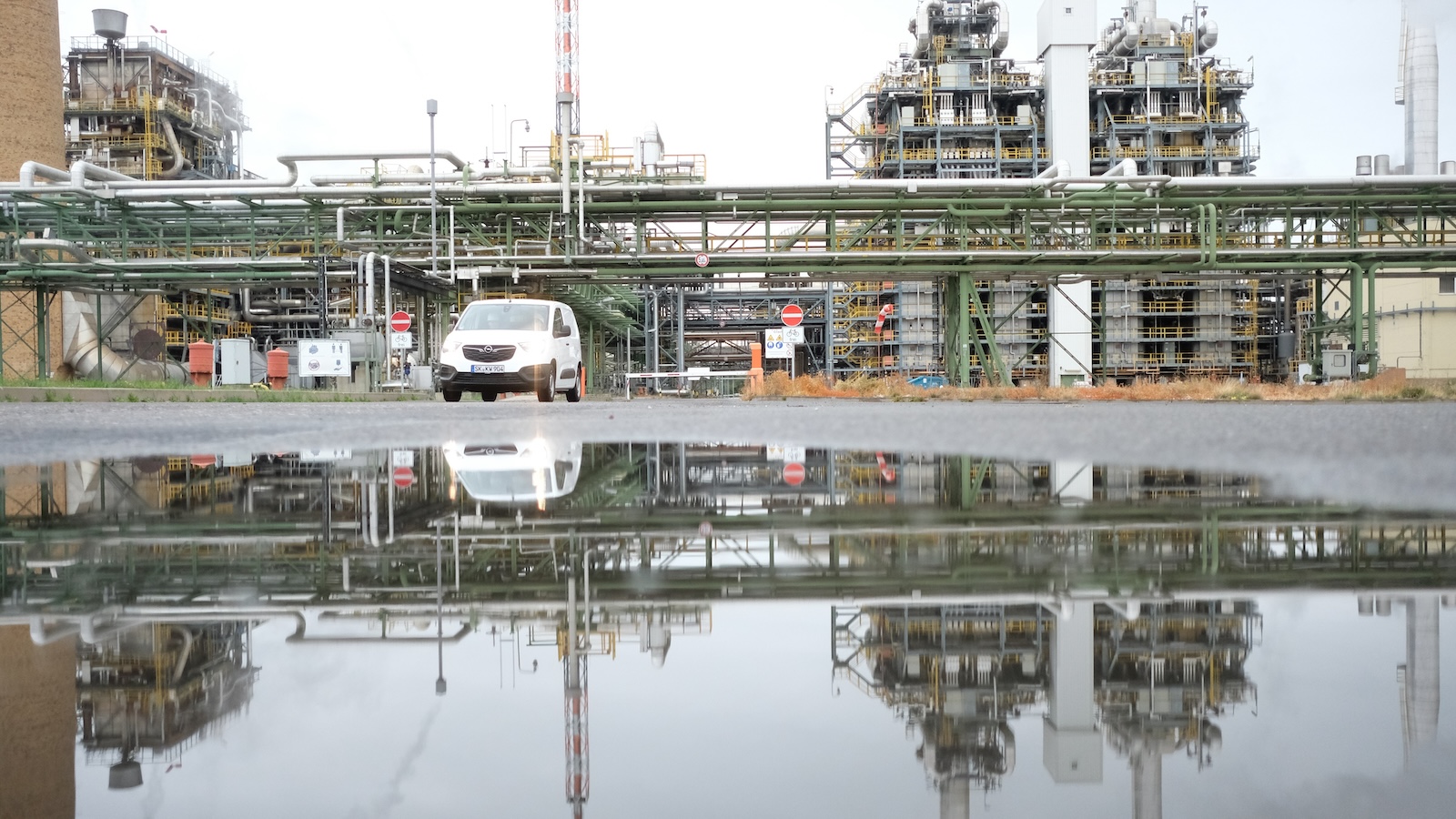 Large factory with car parked outside, and water in foreground