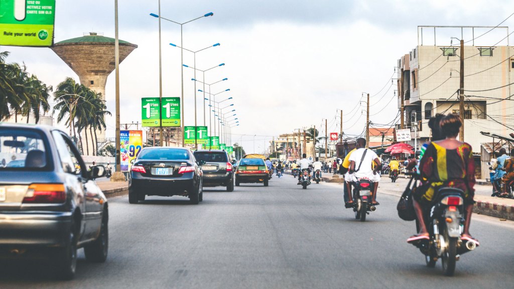 Cars and people on motorbikes driving down a street in Cotonou, Benin, West Africa