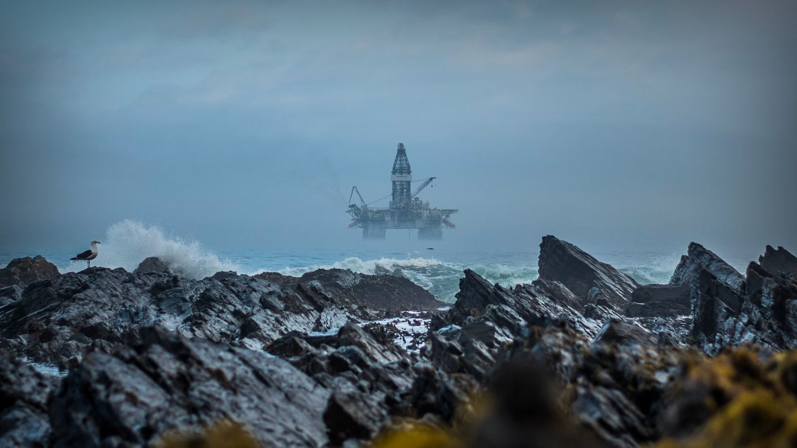 Ominous offshore oil rig with jagged rocks in foreground