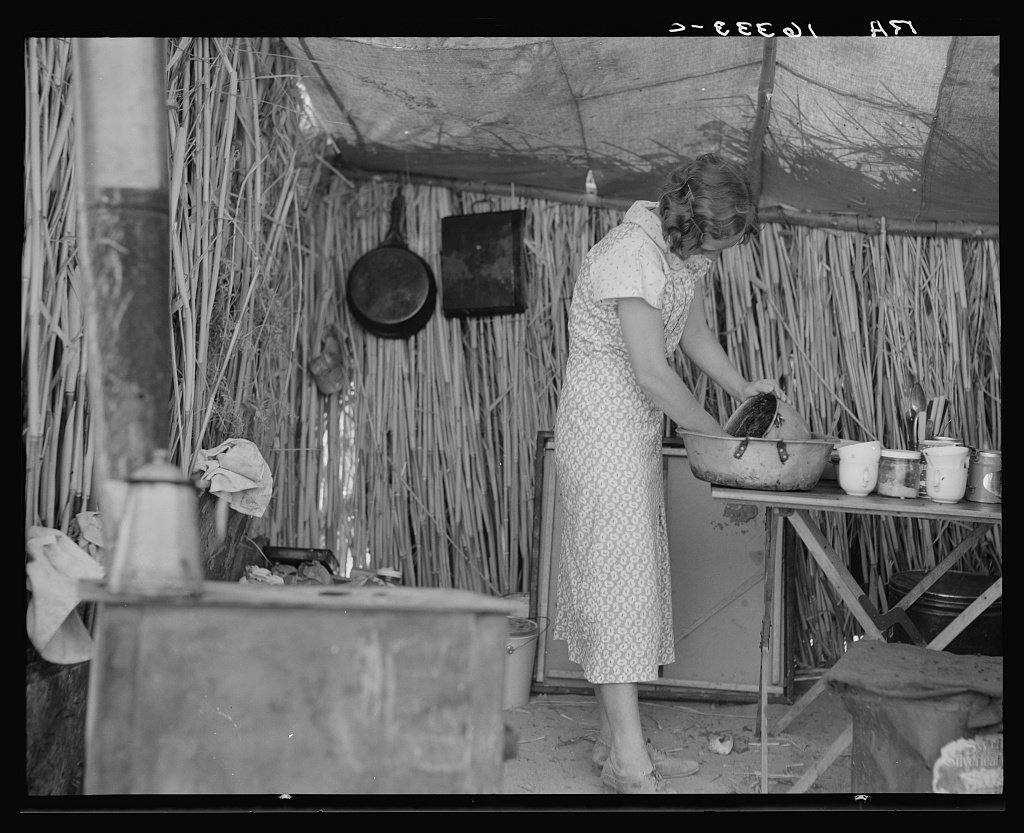 A woman pours water in the kitchen of a shack.