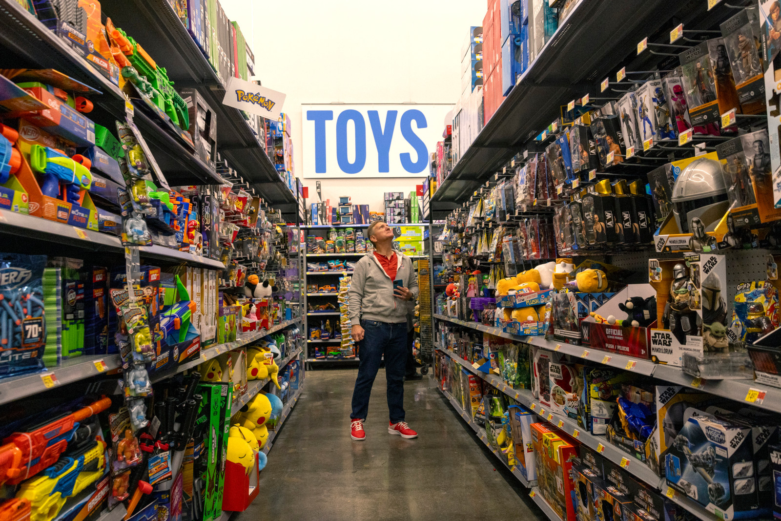 A person wearing a gray zippered hoodie looks up at shelves of toys under a sign that says "TOYS"