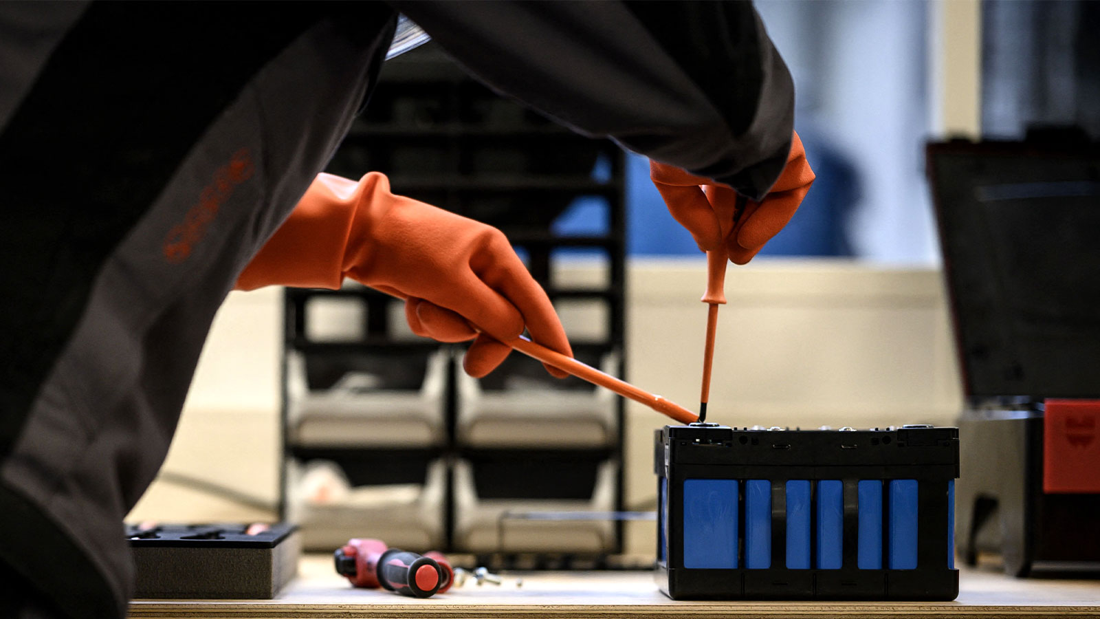 A mechanic wearing orange gloves works on an electric car's battery module