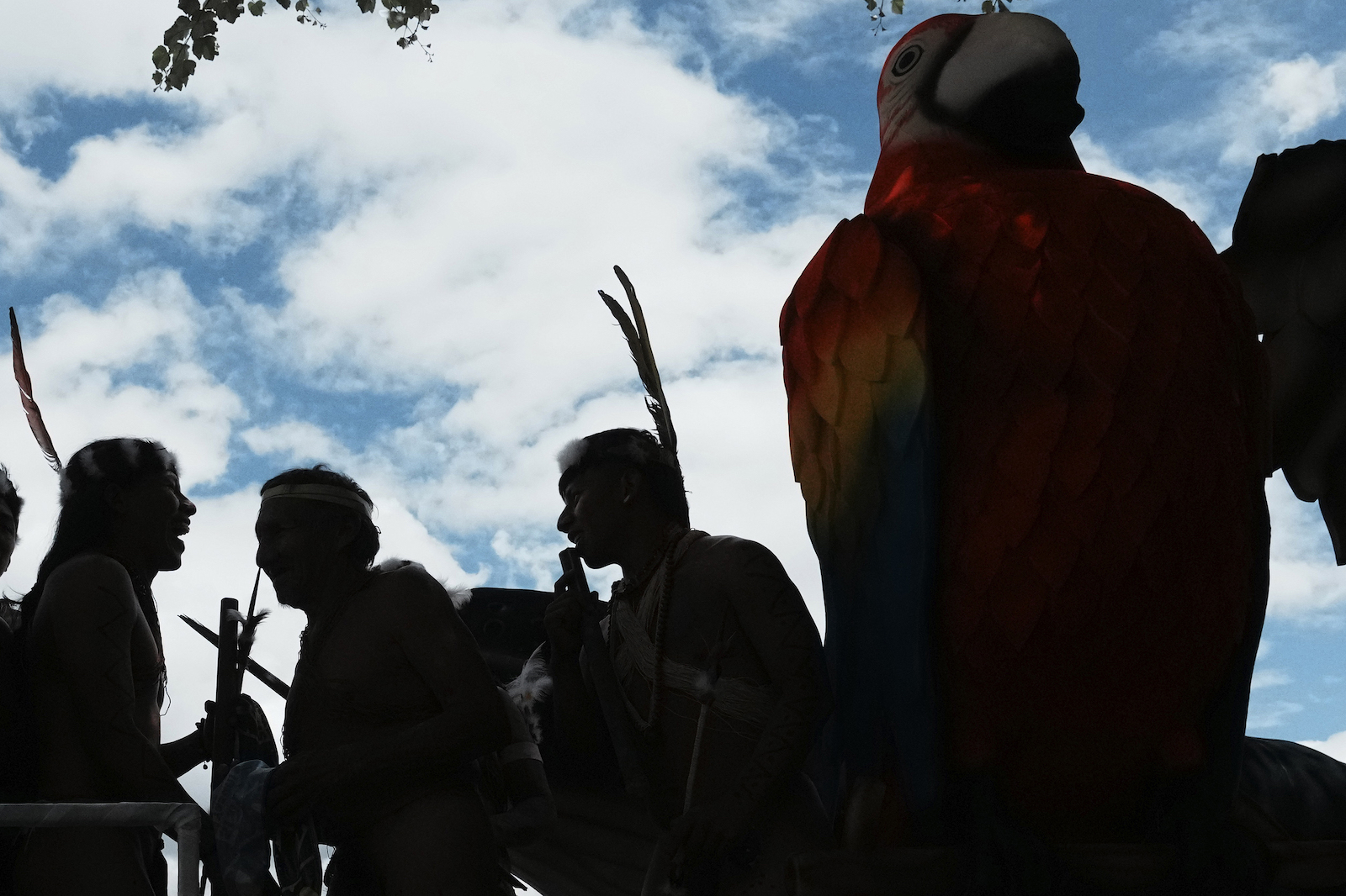 a group of people with tall headdresses silhouetted against blue sky and clouds