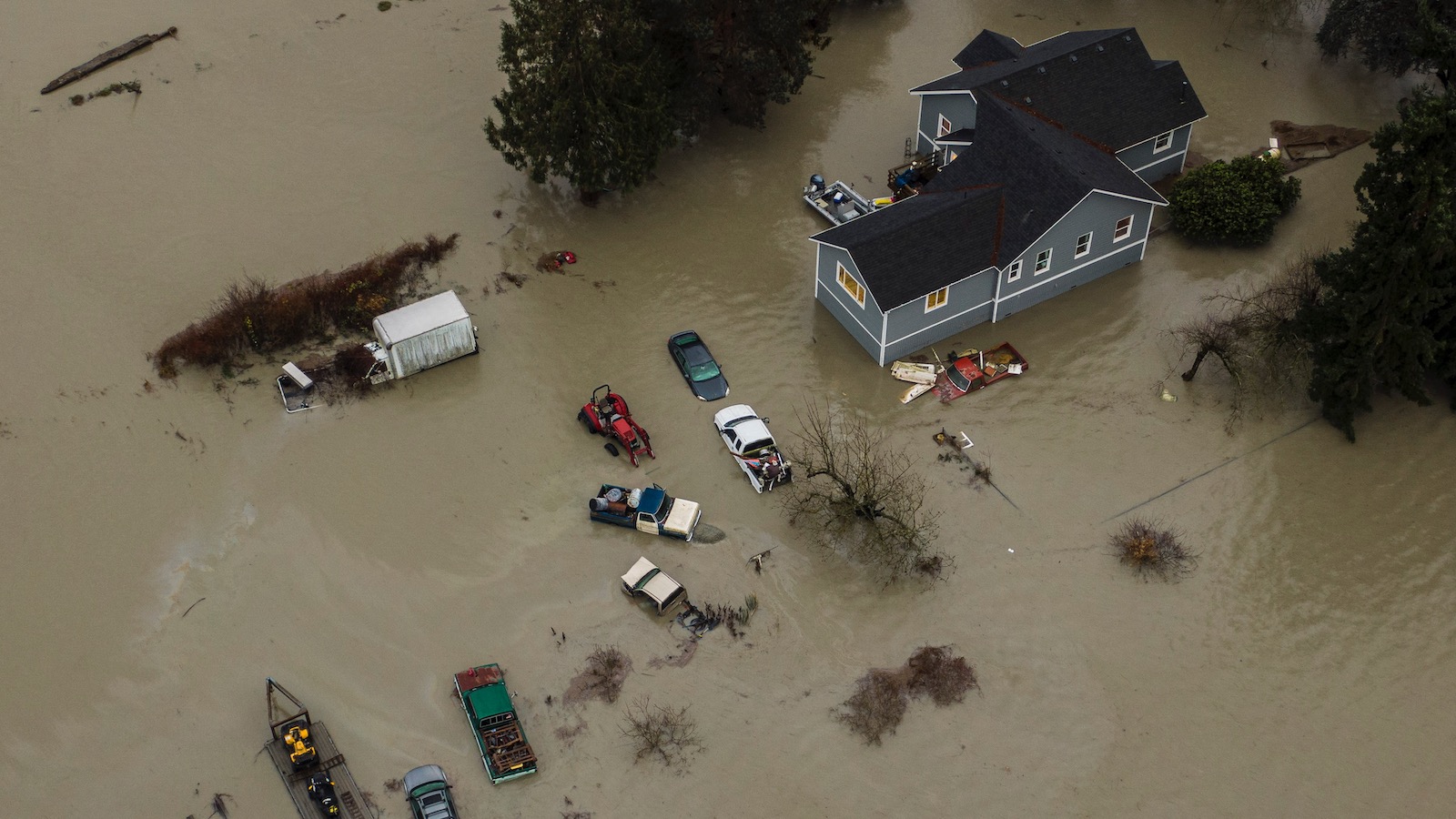 An aerial view shows muddy floodwaters surrounding a home and submerging cars in Stanwood, Washington on December 6, 2023 .