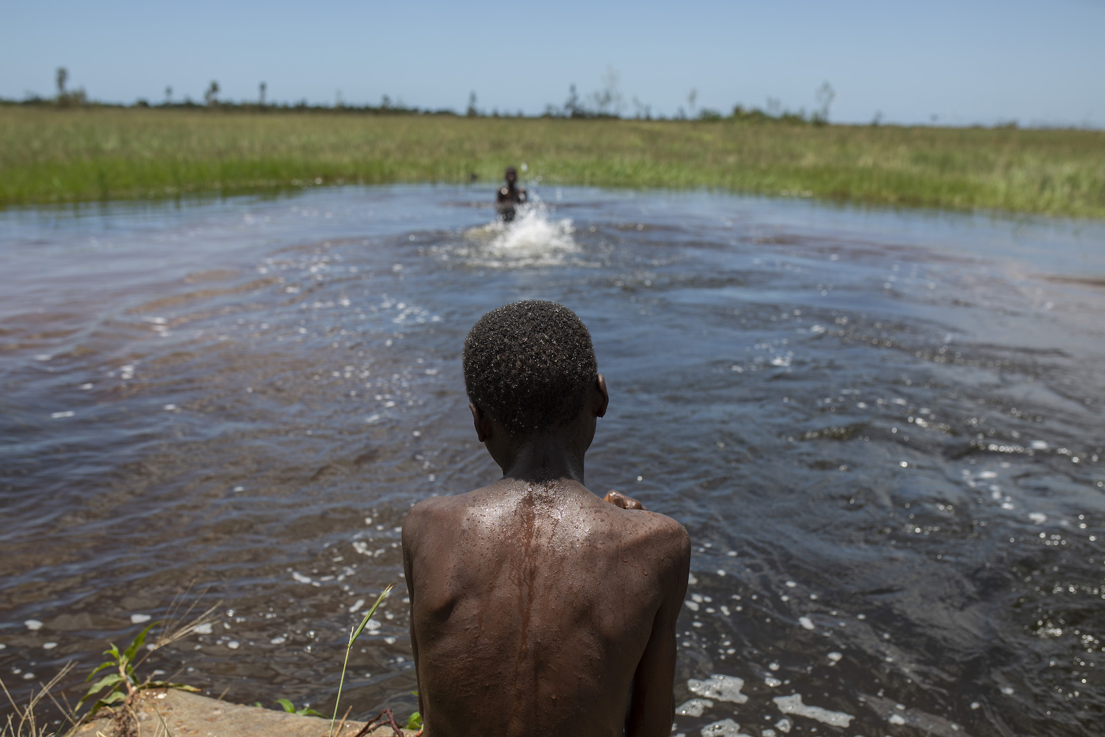 a boy looks at a natural pool with kids playing