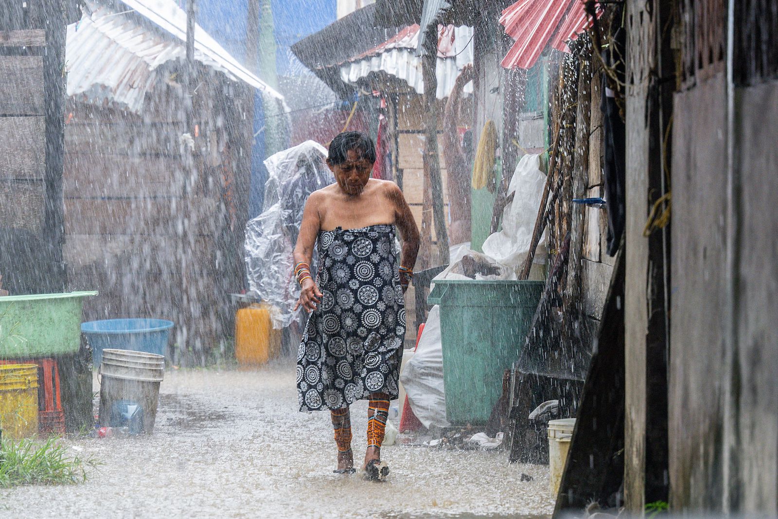 a woman walks through the rain surrounded by dense village housing