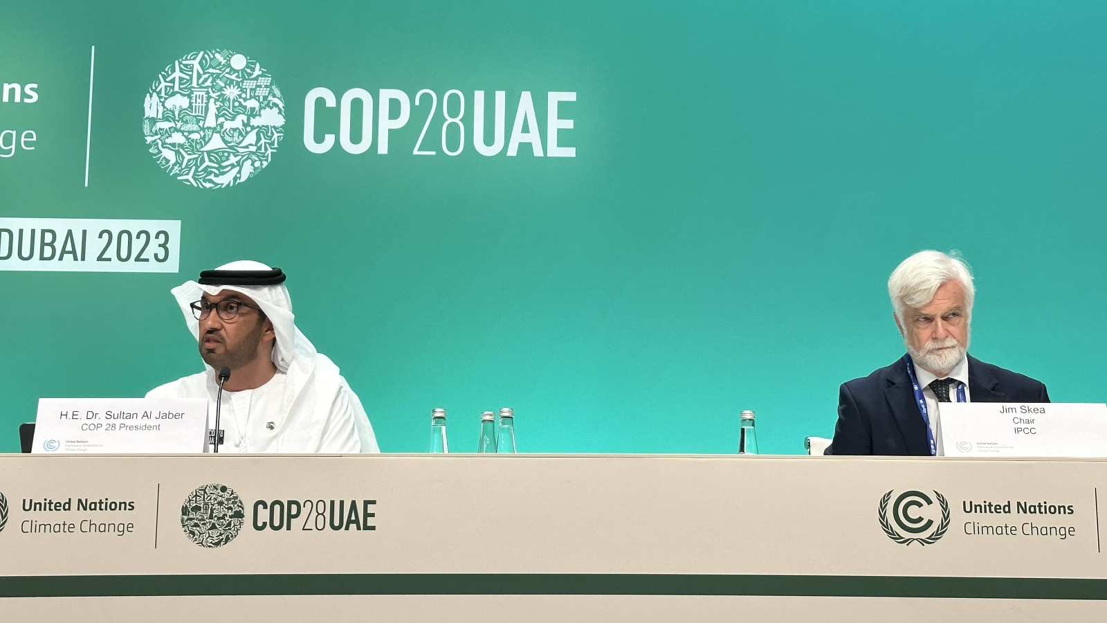 Two men are seated at a panel in front of a green background that says COP28UAE
