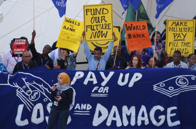 Protesters stand behind banner that reads "Pay up for loss and damage"