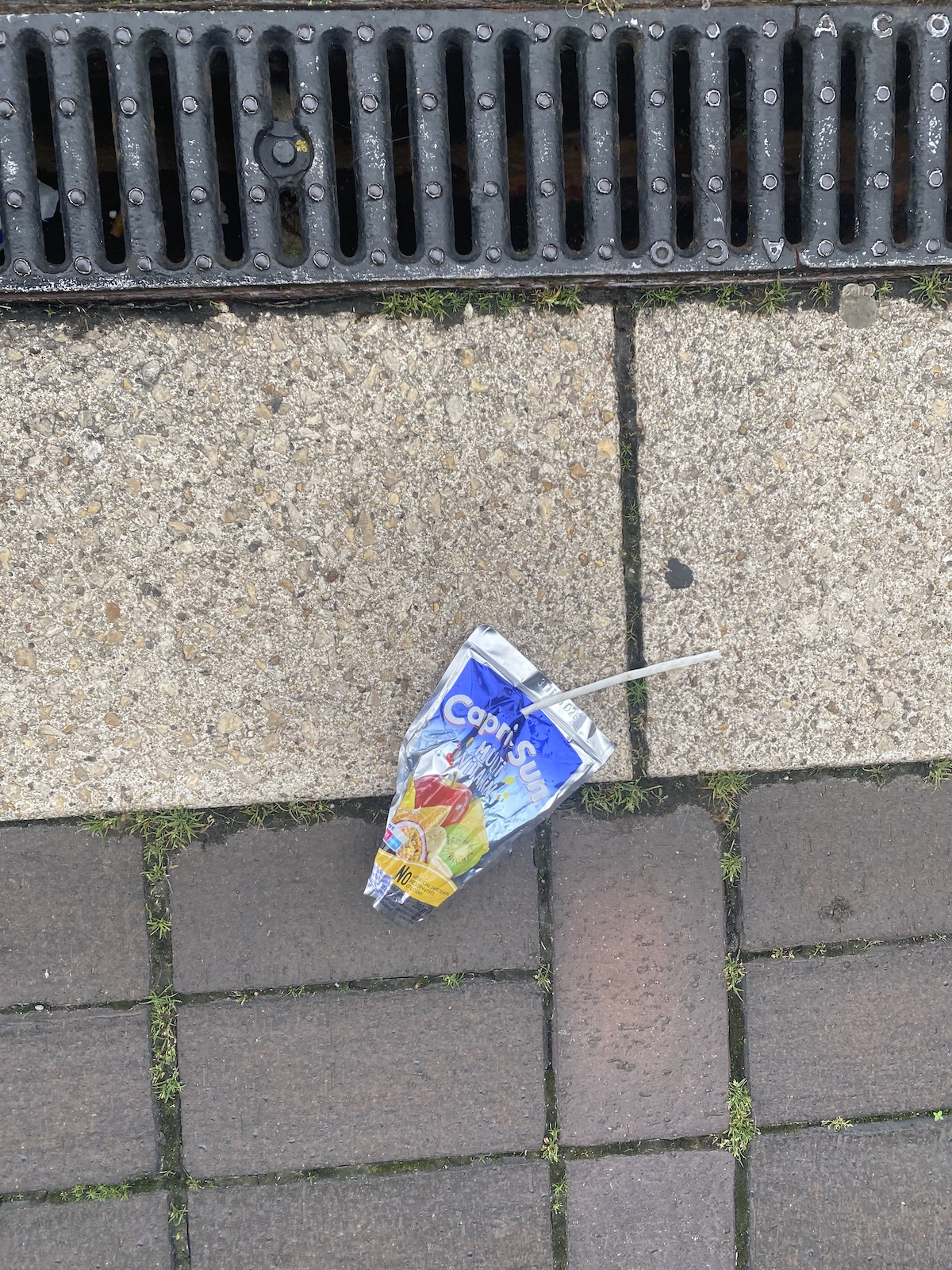 an empty package of capri sun drink on the ground near a grate