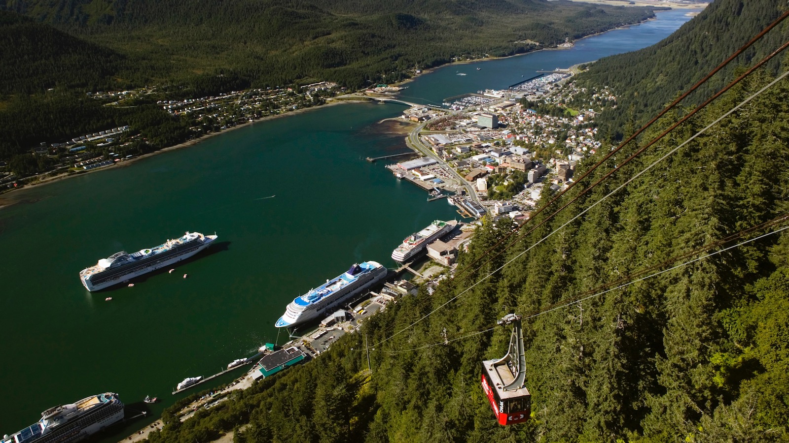 An aerial view of Juneau, Alaska nestled against a mountain with cruise ships on the waterfront.