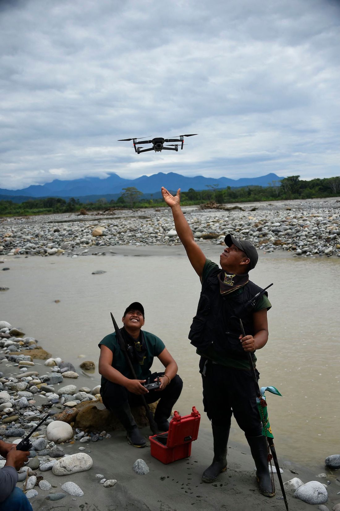 a man holds up his hand doward a small drone plane while another sits on the ground looking up