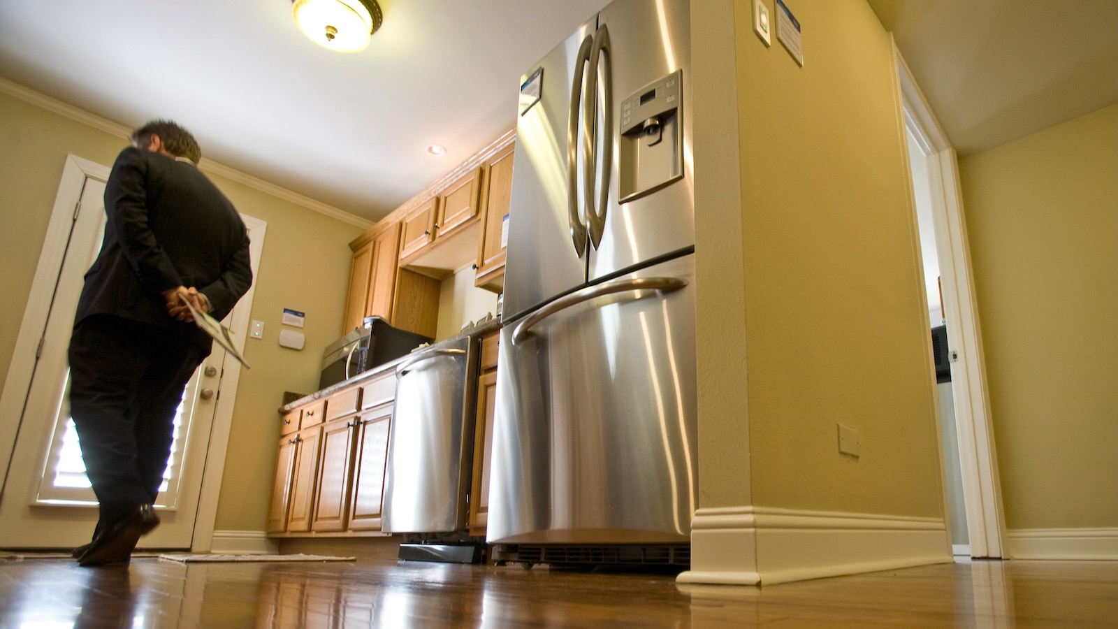 A woman walks through a kitchen with an electric refrigerator and stove.