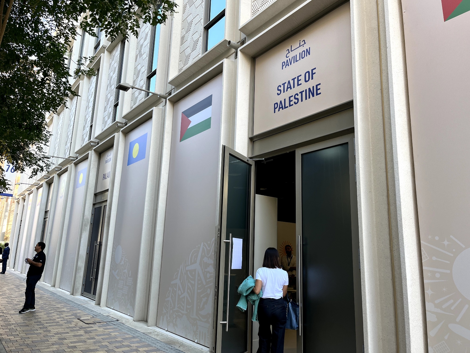 A woman is seen from behind entering the door to a building labeled "Pavilion State of Palestine"