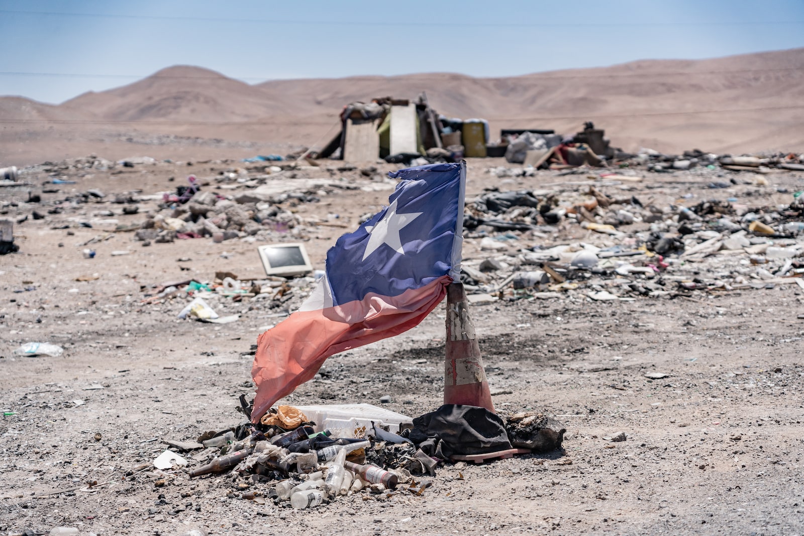 a Chilean flag stands in a traffic cone in the desert among burned piles of garbage