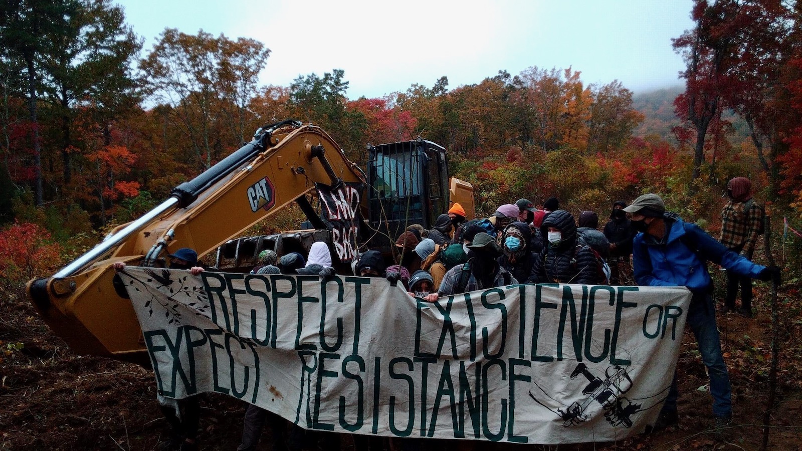 A crowed of protestors gathers behind a banner reading "Respect existence or expect resistance" at a Mountain Valley Pipeline construction site in the mountains of Virginia.