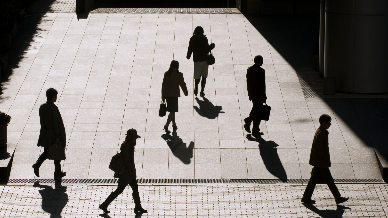 Photo of silhouetted office employees walking with briefcases.