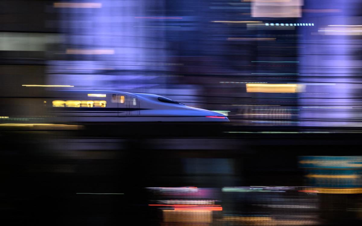 An artfully blurred photo of a train zooming pas a city.