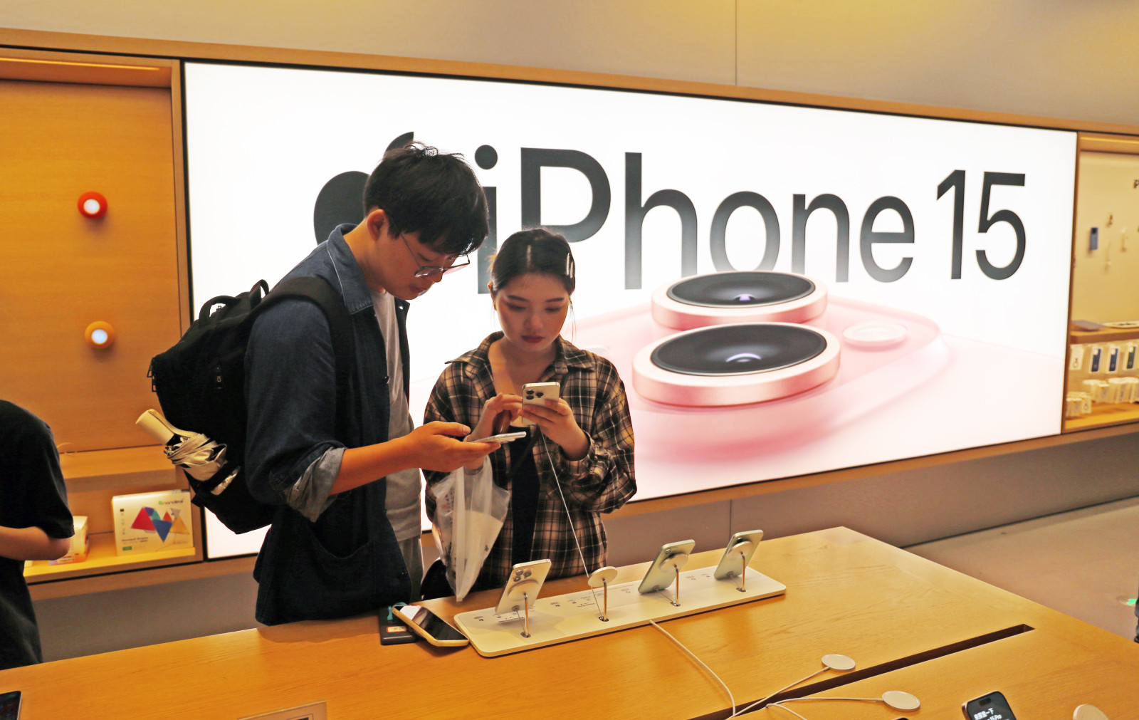 A man and a woman each hold an iPhone inside an Apple Store in front of a sign that says iPhone 15
