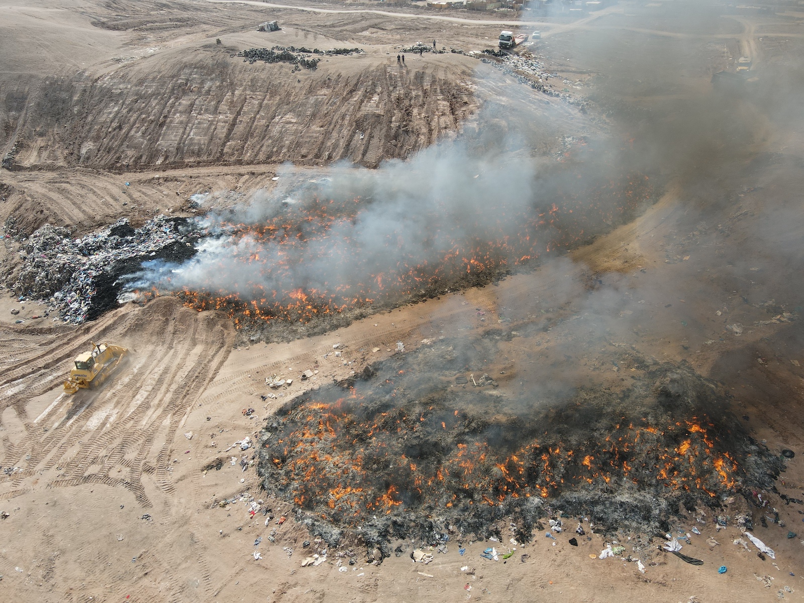 Smoke plumes from burning piles of clothing in sand dunes