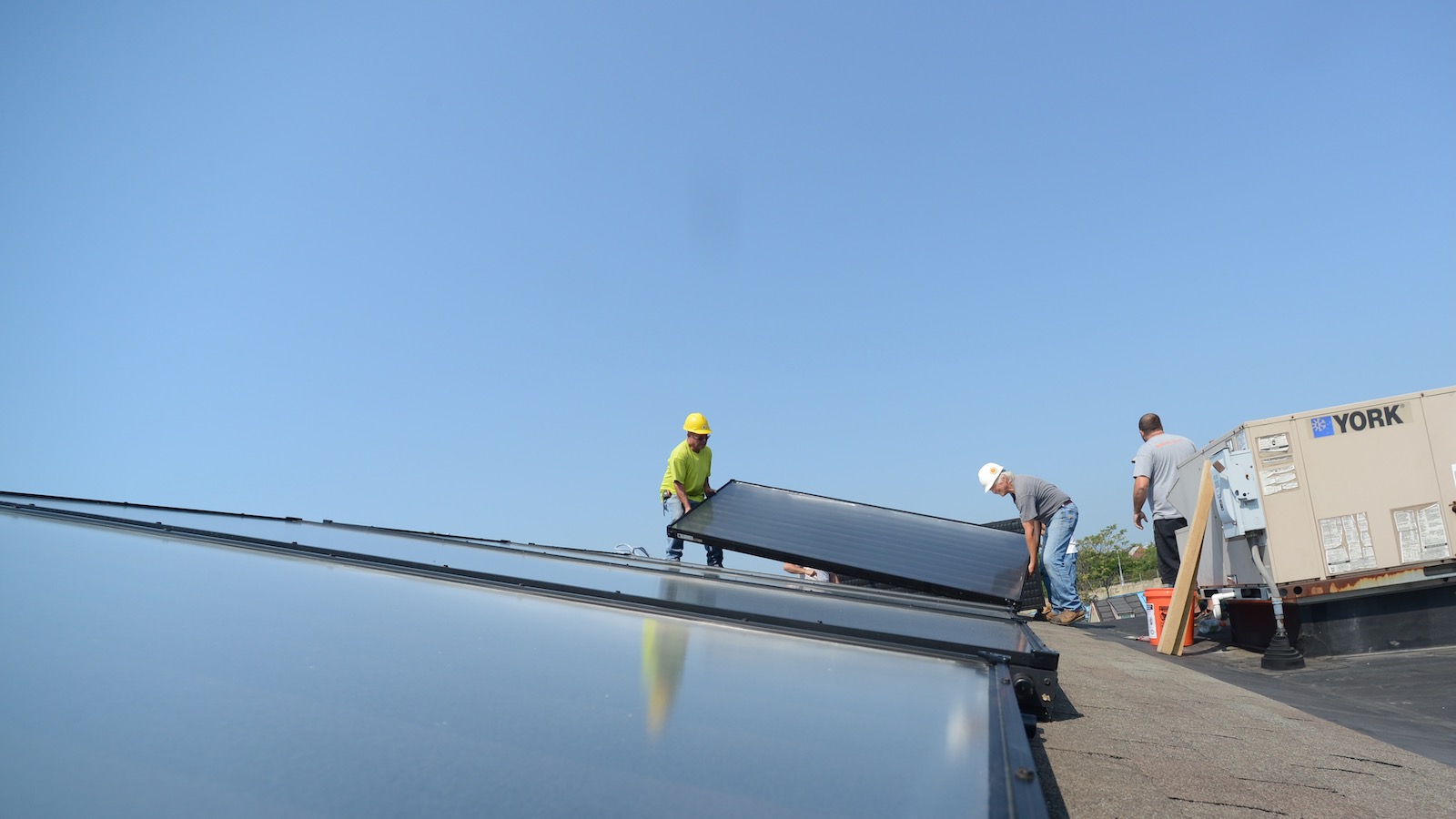 Three workers install solar panels on the roof of a house.