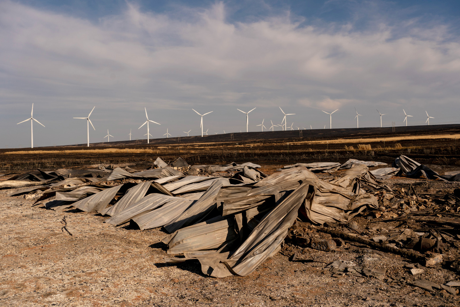 A photo shows rubble from a fire and wind turbines in the distance