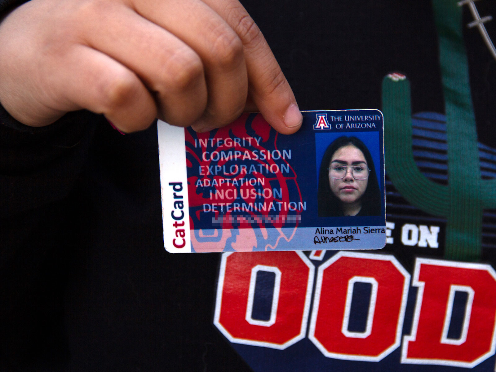 a hand holds a university of arizona ID card with a woman’s photo and the word “CatCard”