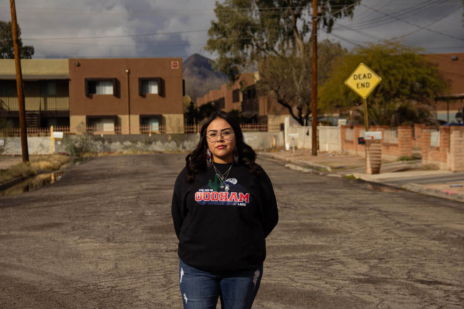 a woman in a black sweatshirt stands near a sign that says "dead end" near a flat-top brick building
