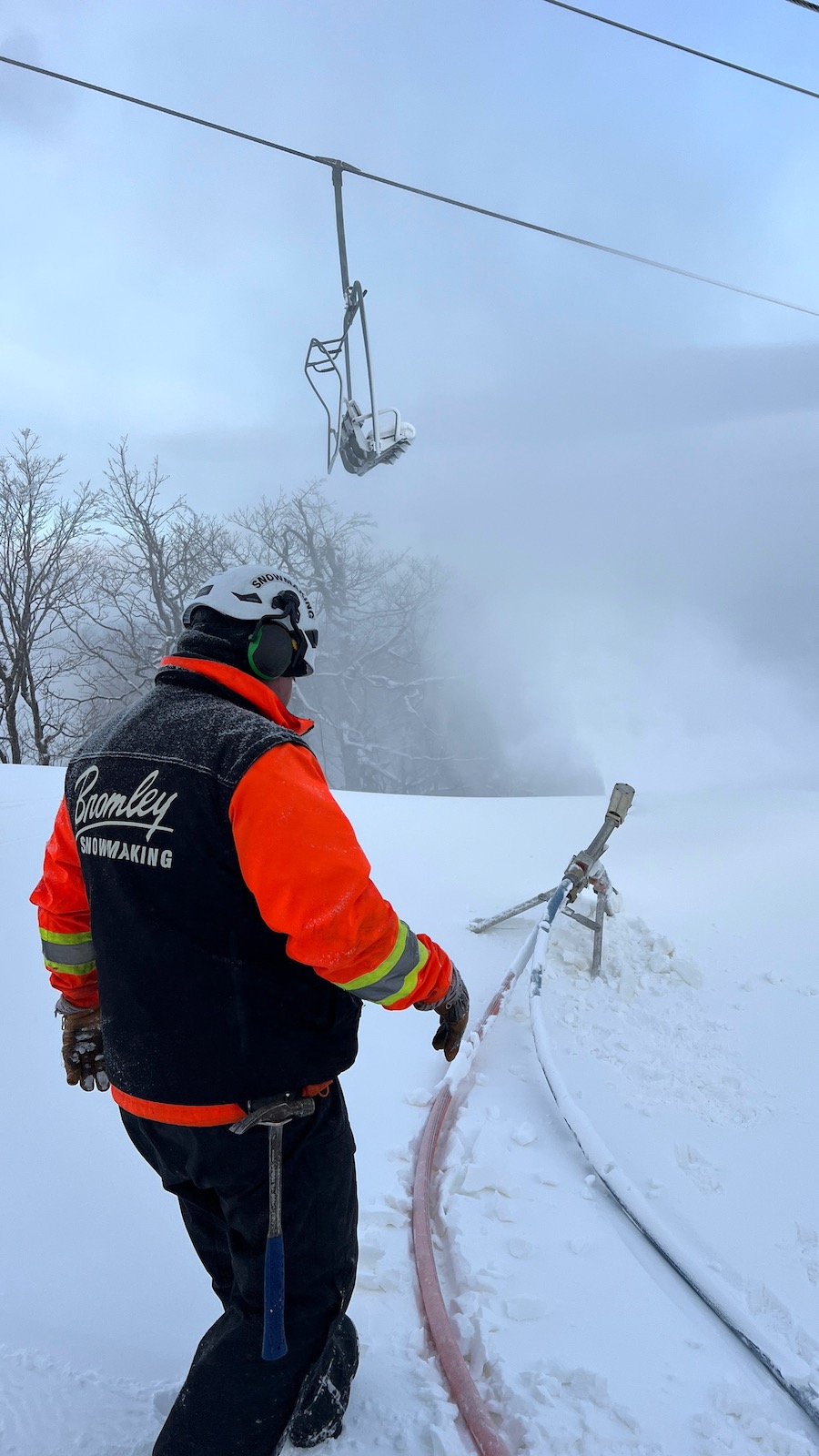 A man wearing thick winter gear checks on a snowgun that is blowing artificial snow on a ski run at Bromley Mountain in Vermont.