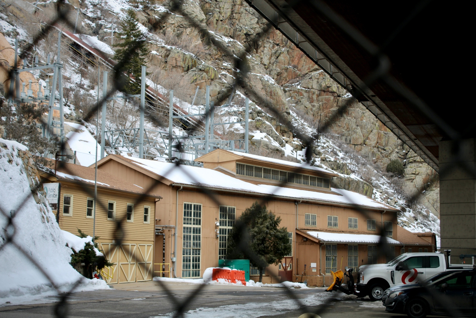 透过铁丝网，可以看到一座被白雪覆盖的棕色建筑。