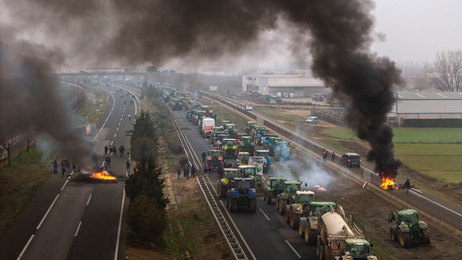 Tractors and burning piles of burning agricultural waste block a highway during a farmers protest in Spain