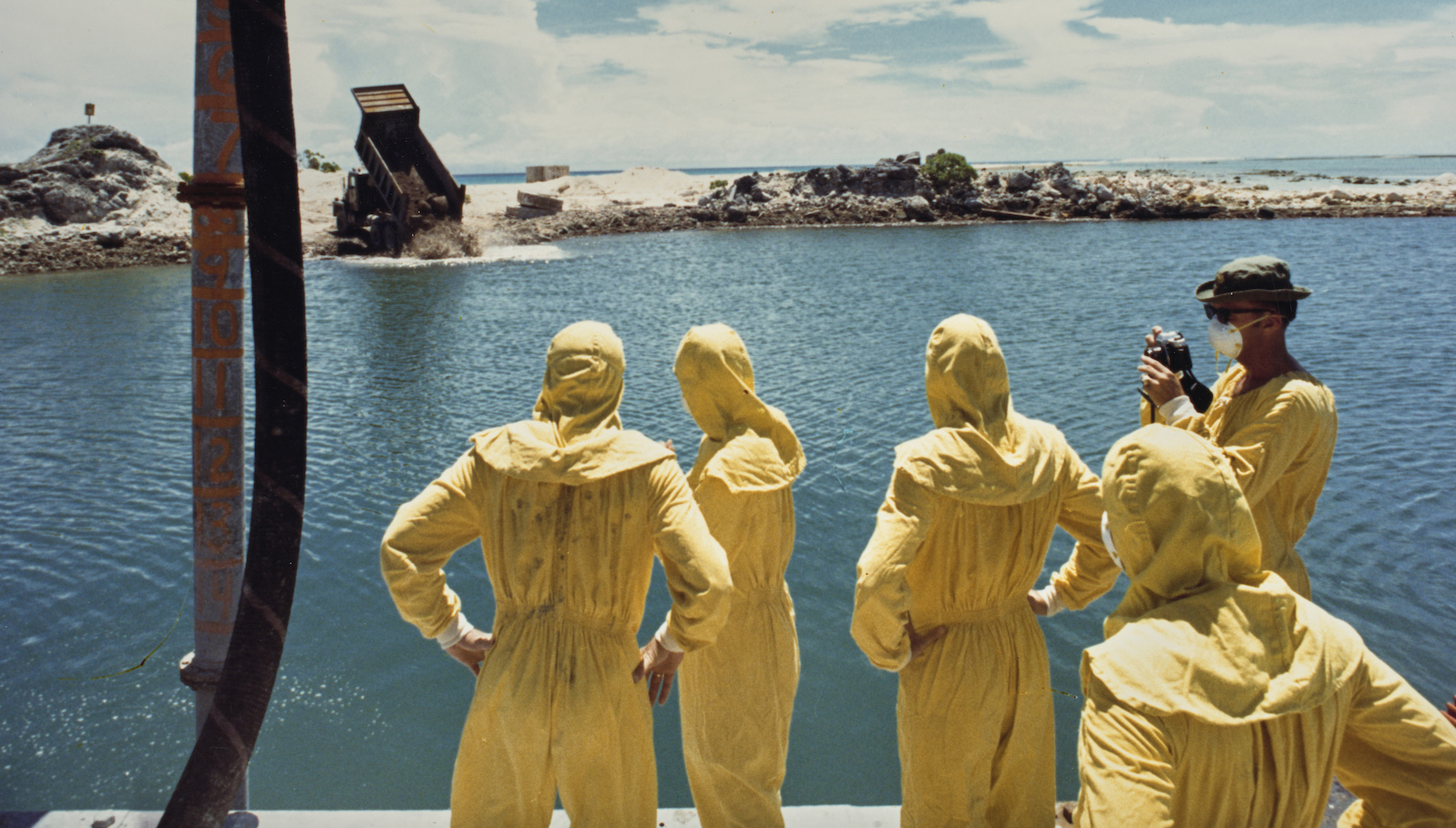 German-born American military officer Herbert E Wolff and military personnel of the 84th Engineers Battalion, 45th Support Group, USASCH, each wearing protective yellow coveralls as they watch as hardened concrete mixed with contaminated soil and attapulgite additive being dumped from a 20-ton truck into the crater formed by a nuclear bomb, on the northern tip of Runit Island, one of forty islands of the Enewetak Atoll, Marshall Islands, 26th July 1978. Runit Island is a dumping ground for radioactive waste left by the United States after it conducted a series of nuclear tests on Enewetak Atoll between '46 and '58. (Photo by Department of Defense/US Army/FPG/Archive Photos/Getty Images)