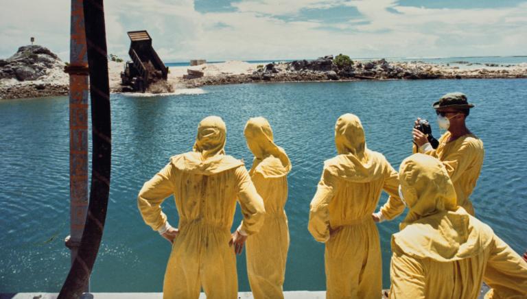 German-born American military officer Herbert E Wolff and military personnel of the 84th Engineers Battalion, 45th Support Group, USASCH, each wearing protective yellow coveralls as they watch as hardened concrete mixed with contaminated soil and attapulgite additive being dumped from a 20-ton truck into the crater formed by a nuclear bomb, on the northern tip of Runit Island, one of forty islands of the Enewetak Atoll, Marshall Islands, 26th July 1978. Runit Island is a dumping ground for radioactive waste left by the United States after it conducted a series of nuclear tests on Enewetak Atoll between '46 and '58. (Photo by Department of Defense/US Army/FPG/Archive Photos/Getty Images)