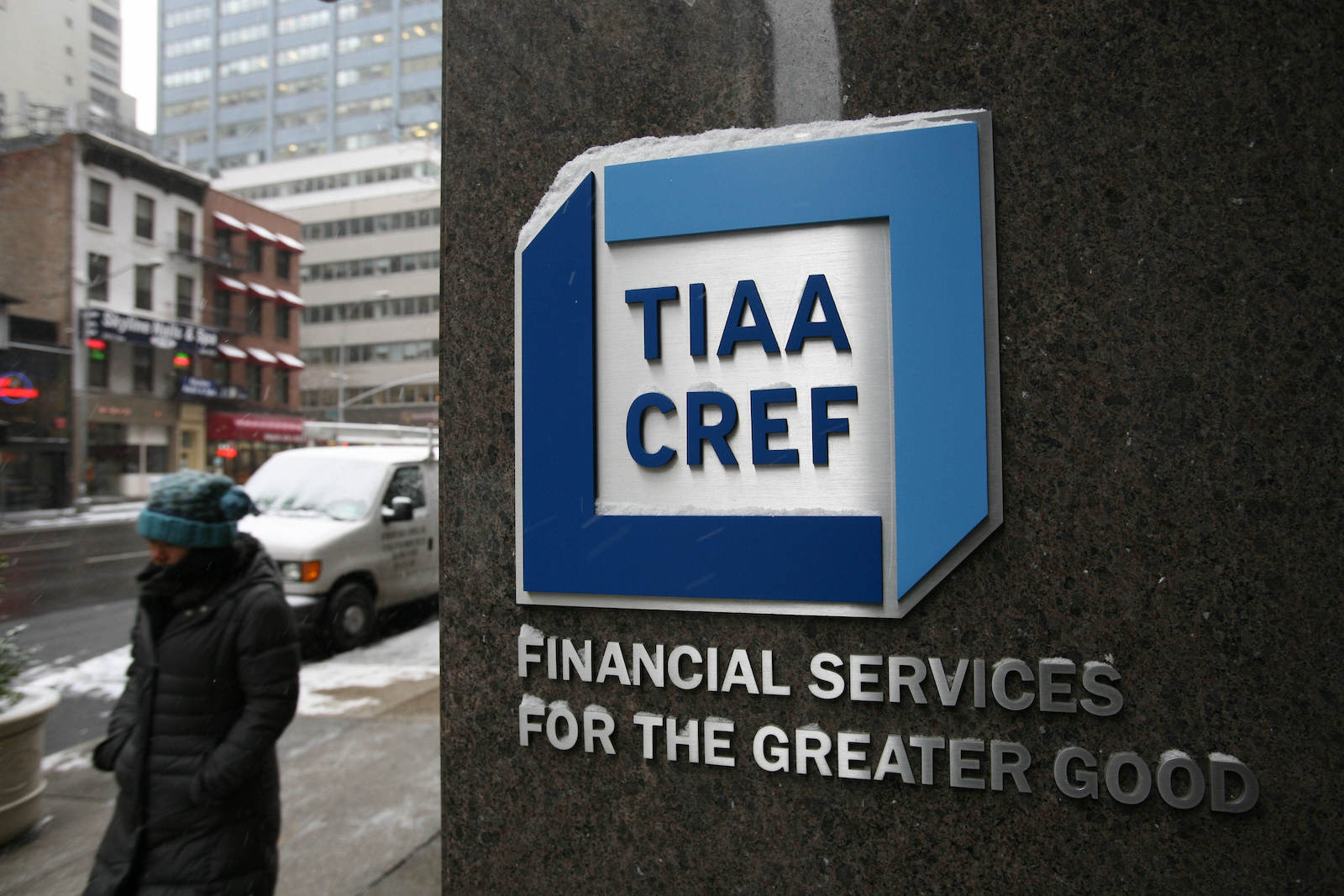 a winter-bundled person walks by a building with a logo for TIAA CREF with the words underneath it "financial services for the greater good"