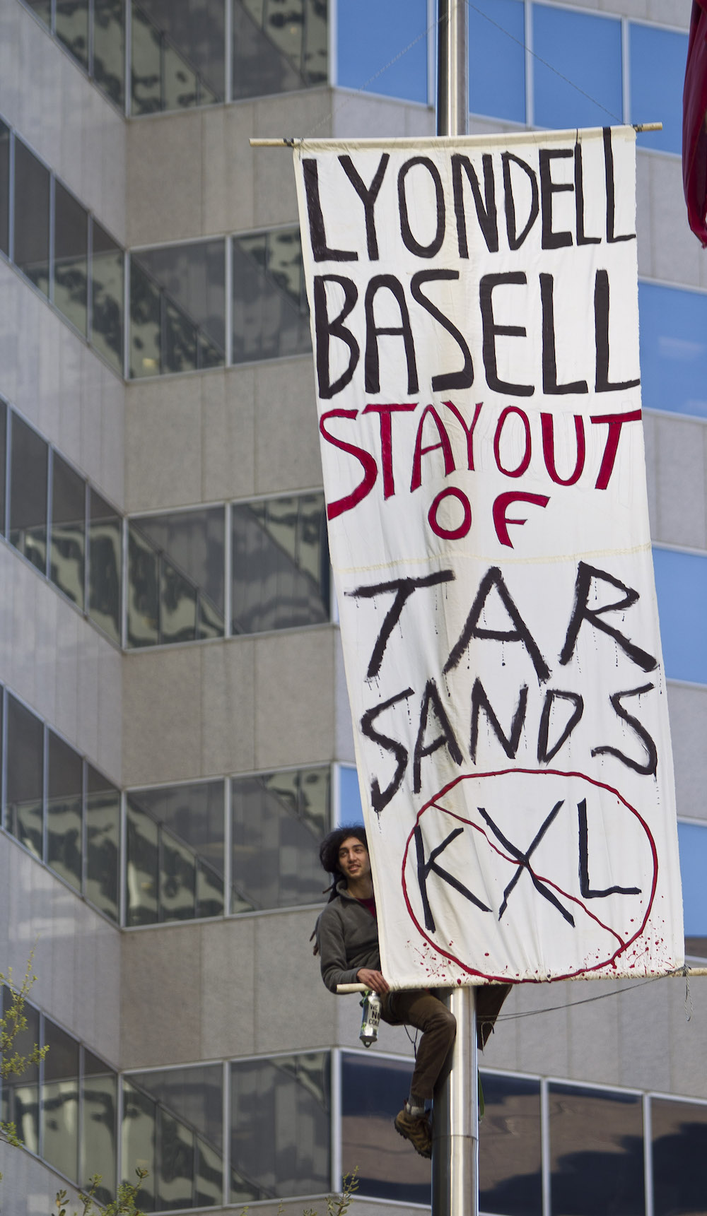 A man climbs a poll to hang a sign saying Lyondell Basell stay out of tar sands
