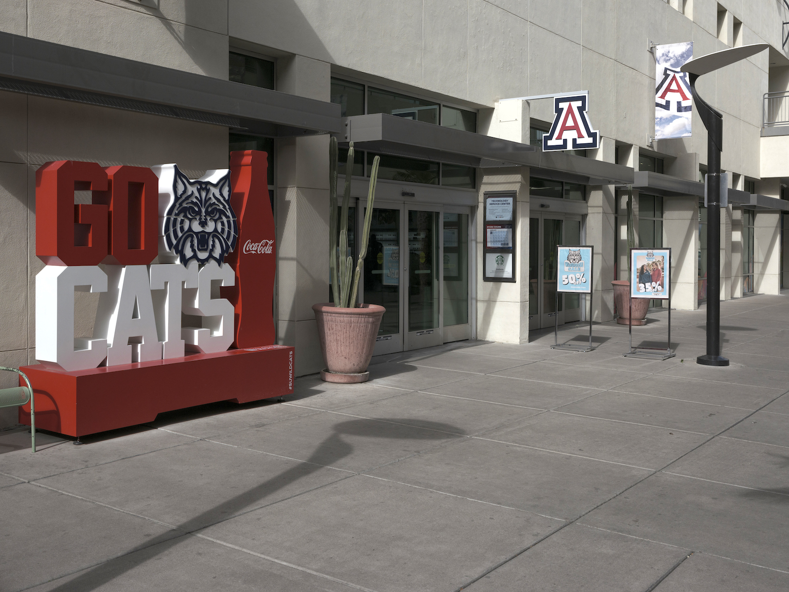 a red Arizona Wildcats mascot structure near a building entrance with University 