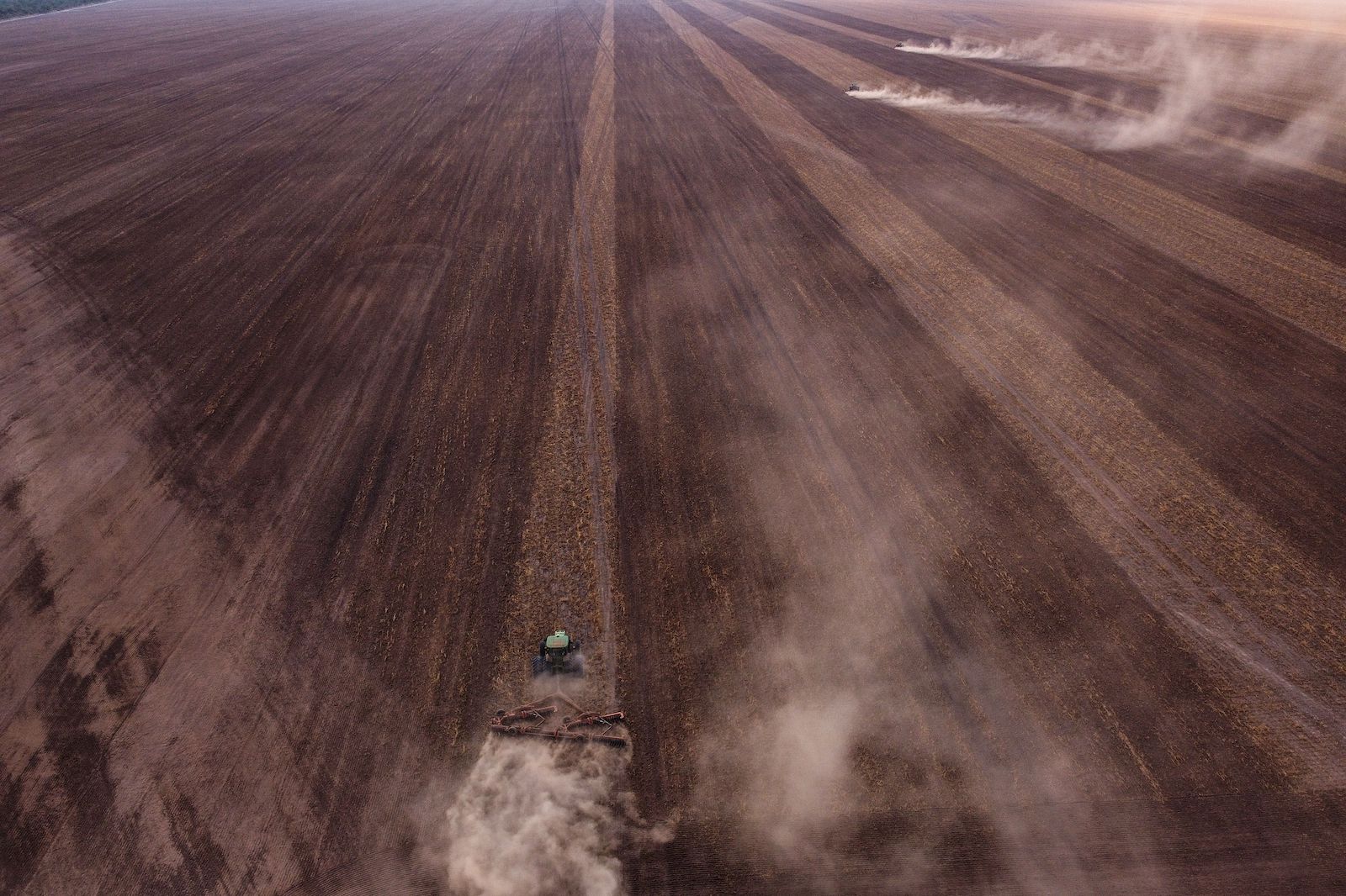 A tractor drives along a long stretch of dry agricultural land