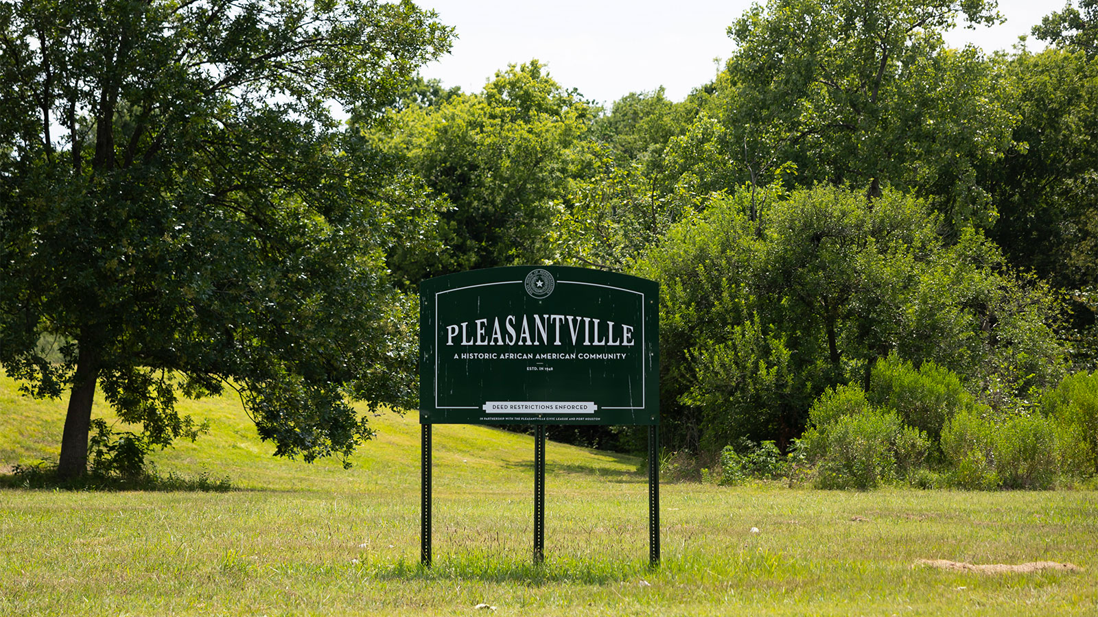 a sign that reads "Pleasantville, a historic African-American community" in a grass field with trees in the background